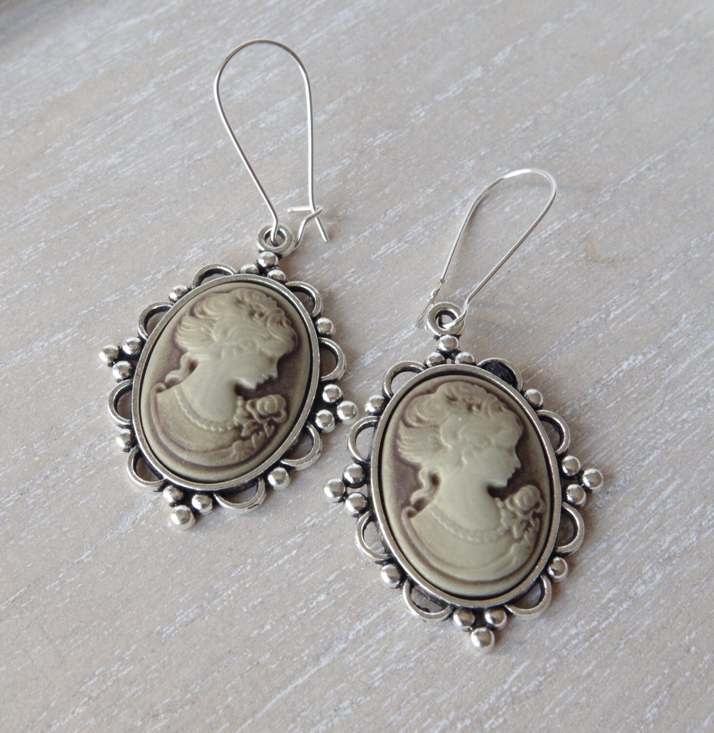 Vue rapprochée de longues boucles d’oreilles au style victorien avec pendentif camée représentant une femme de profil, rehaussé d’un petit nœud décoratif. Teinte bronze patinée, ambiance élégante, fond neutre pour souligner la finesse artisanale du bijou.