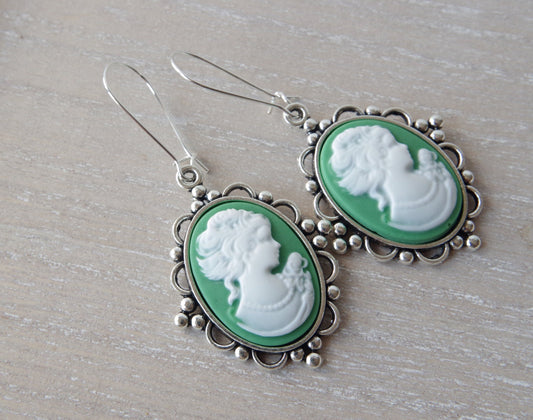  boucles d’oreilles pendantes avec camée rose ovale et profil féminin ivoire, finition bronze antique, posées sur un fond romantique clair. Mise en valeur du style vintage et du raffinement artisanal.