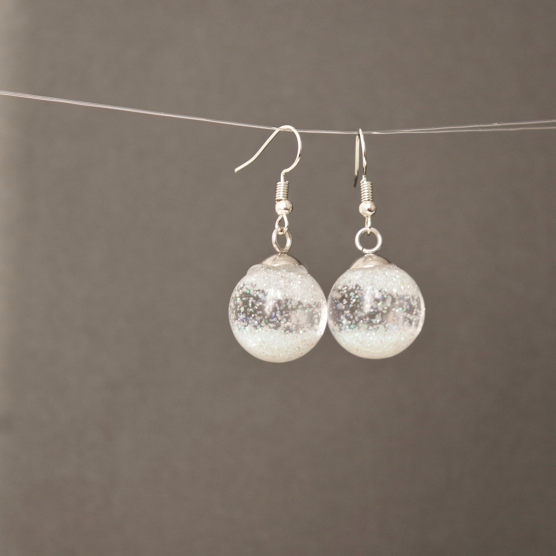 Boucles d’oreilles globe en verre transparent avec flocons de neige en suspension, effet boule à neige, bijou hivernal élégant pour femme.