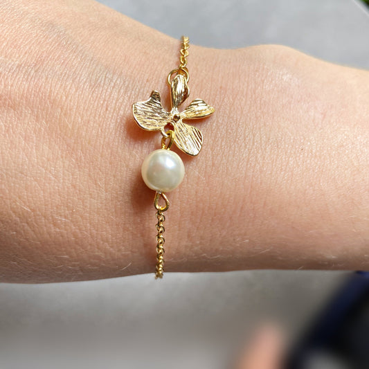 Fleur d’élégance – bracelet doré avec orchidée détaillée et perle ivoire en verre, longueur 16 cm avec chaîne d’ajustement pour un porté sur-mesure.